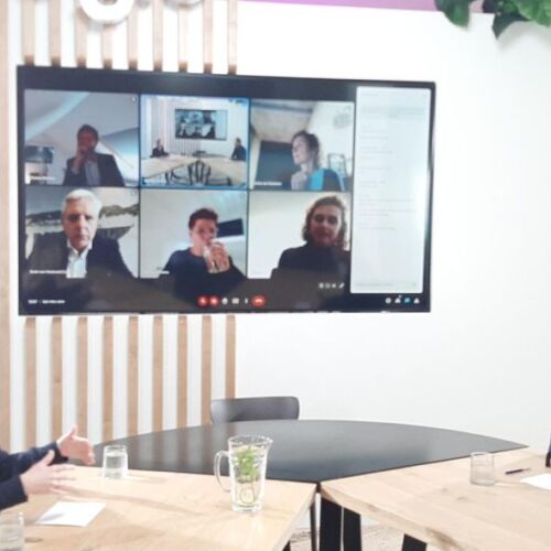 2 mensen aan tafel in gesprek met andere mensen via een live videoverbinding